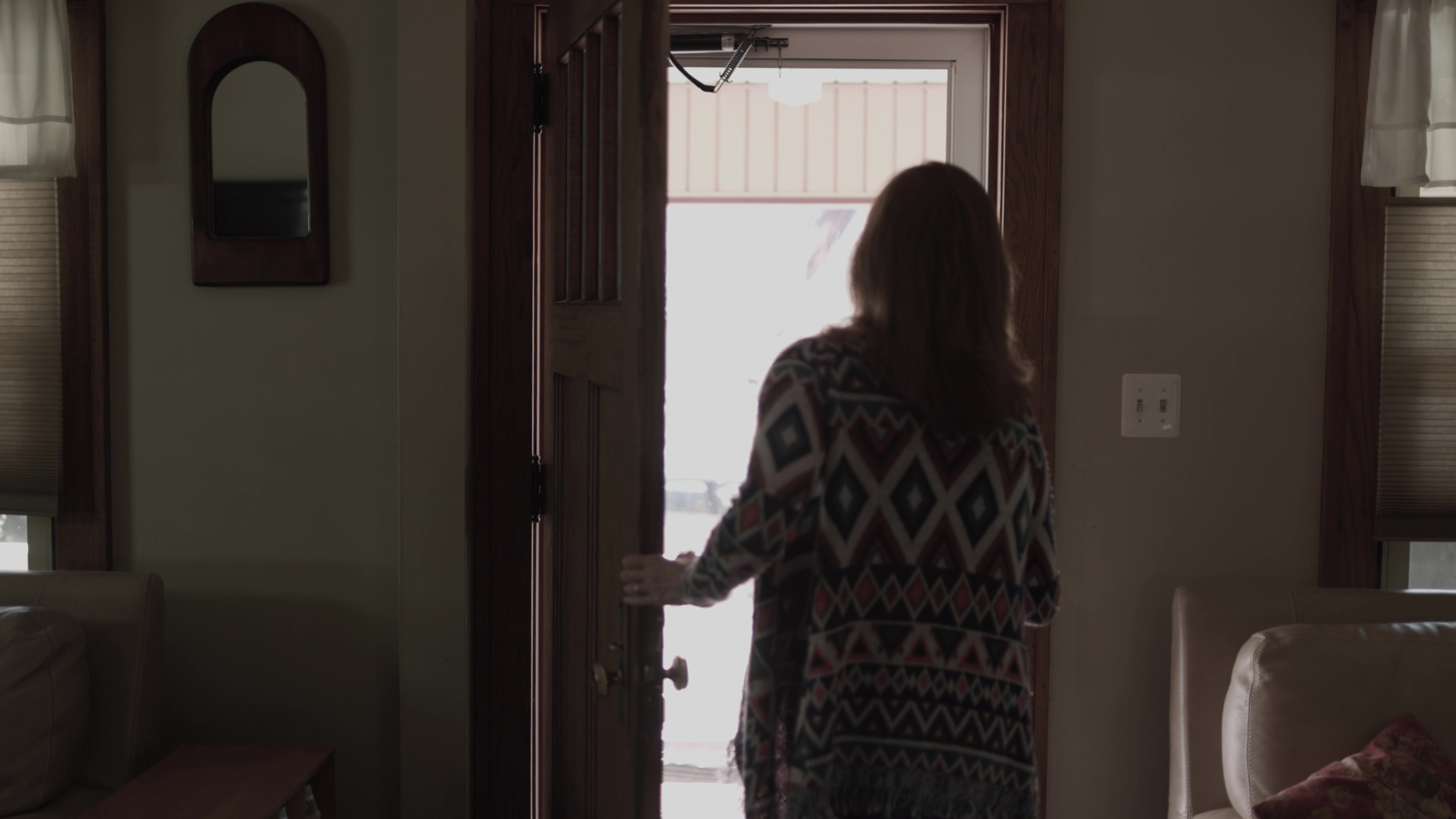 Mary holding her front door open and looking outside